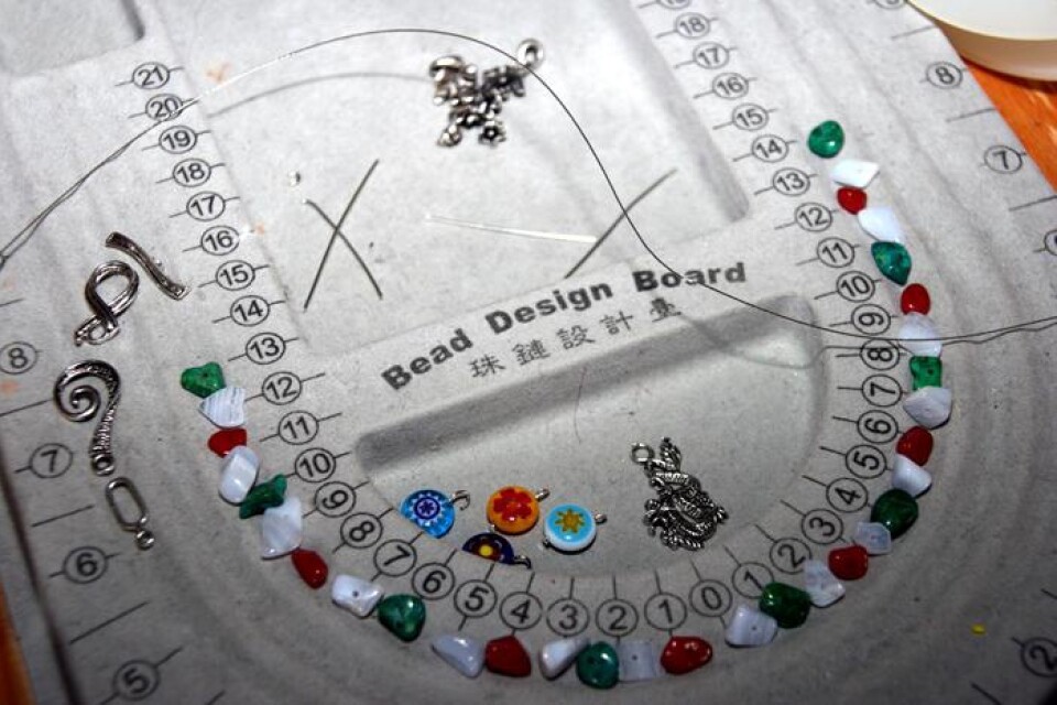 En "bead design board" (bead=pärla/sten/berlock) behövs för att trä halsbanden lika på båda sidor.