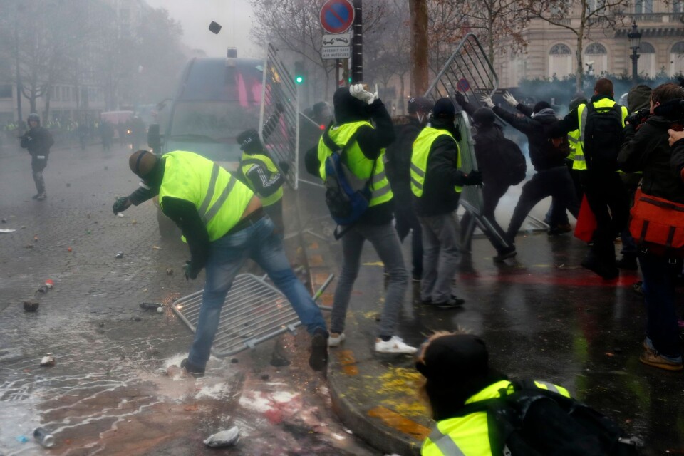 Demonstranter kastar avspärrningsstaket mot en polisbil nära Champs-Élysées.