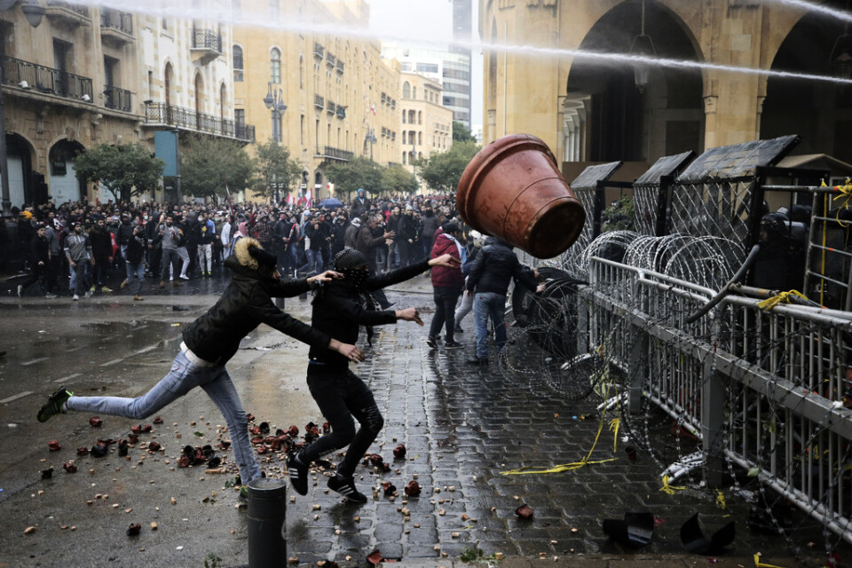 Demonstranter hivar en stor blomkruka mot poliser bakom en avspärrning vid parlamentet.