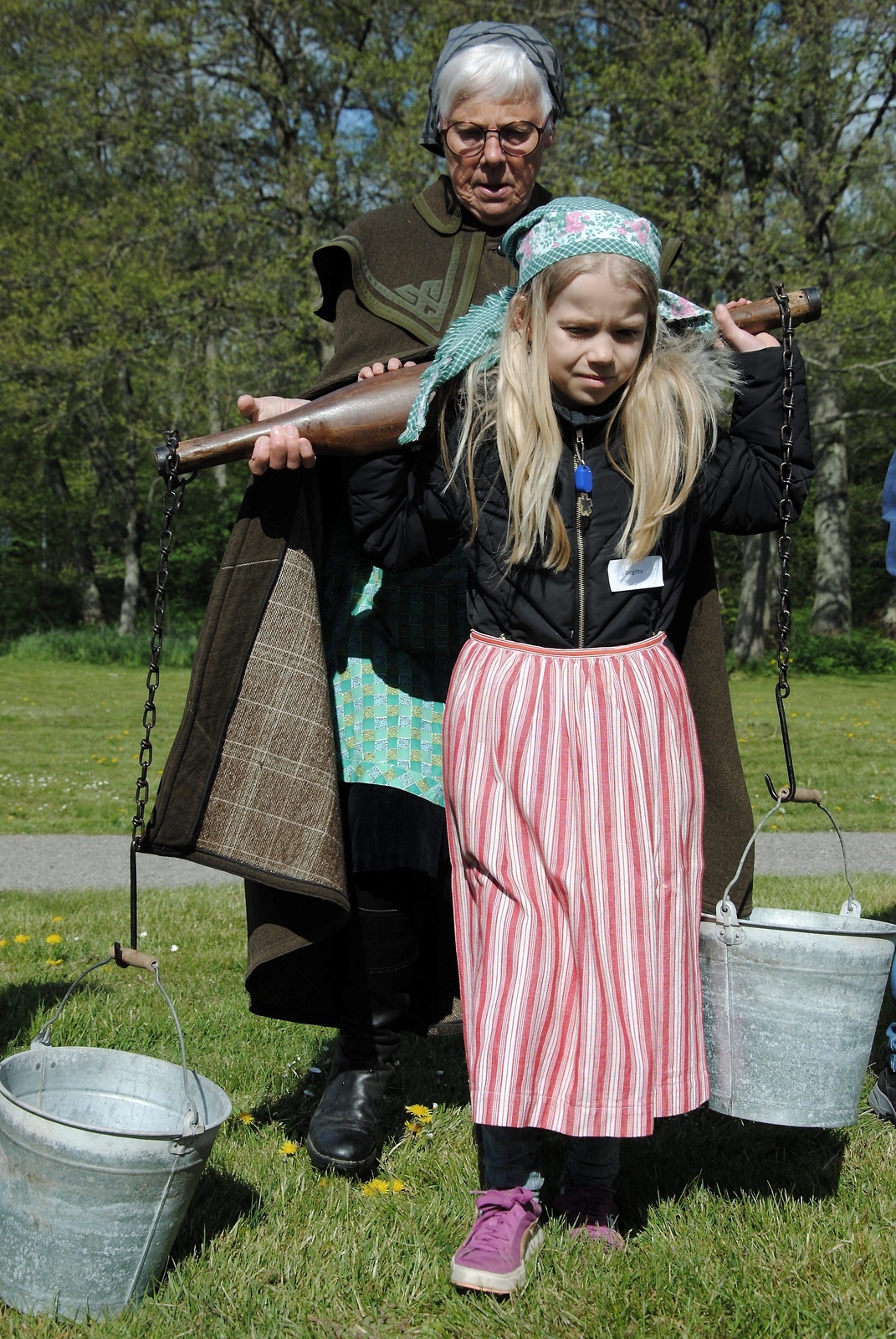 Tindra Arvidsson fick ta i när hon skulle bära två hinkar med vatten. Karin Svensson från hembygdsföreningen förklarade hur hon skulle göra. Foto: Pernilla Ekdahl