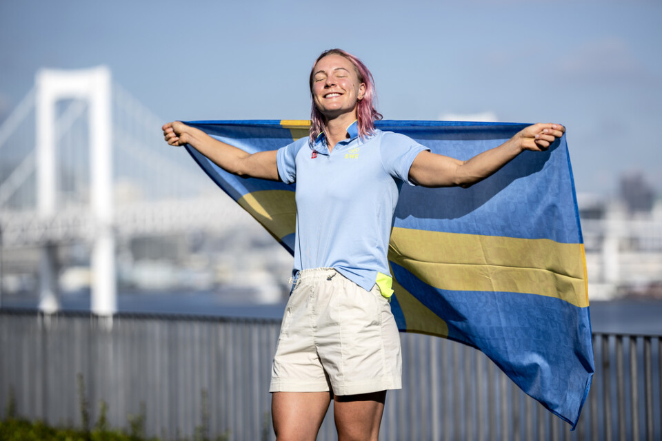 Sarah Sjöström med en svensk flagga och regnbågsbron i Tokyo i bakgrunden.