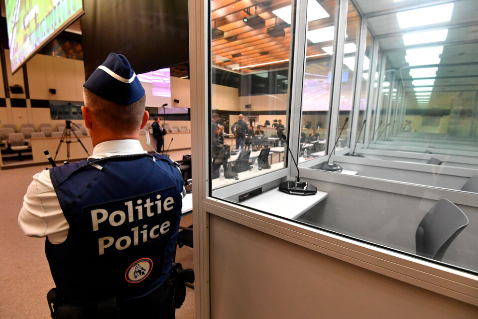 En polis vaktar intill båsen för de anklagade i den rättssal där rättegången kring terrordåden i Bryssel den 22 mars 2016 nu inleds.