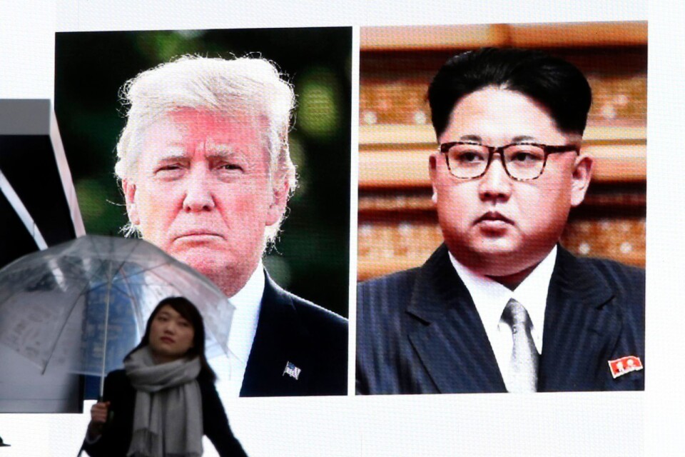 En kvinna går förbi en stor skärm som visar bilder på USA:s president  Donald Trump och Nordkoreas Kim Jong-Un.