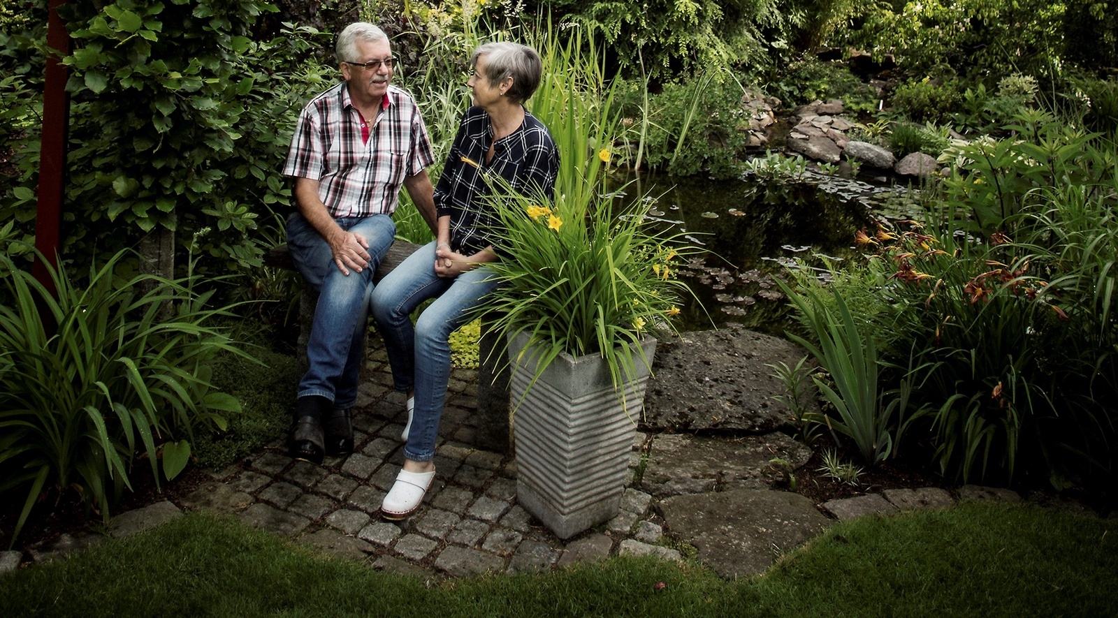 Kaj och Marguerite Nordkvist sitter vid dammen som gömmer sig på trädgårdens baksida.