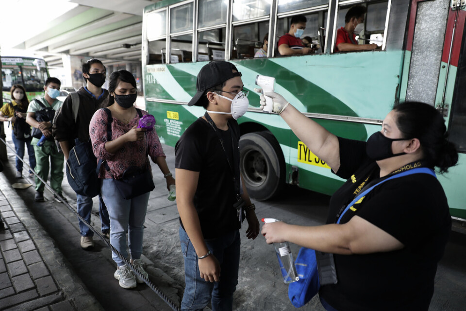 Passagerare får sin kroppstemperatur kontrollerad innan de går ombord en buss under den första dagen av lättade restriktioner i Manila på måndagen.