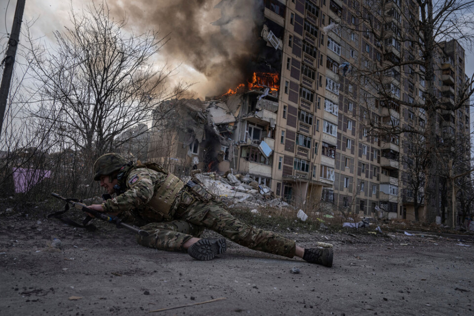 En ukrainsk polis kastar sig för att ta skydd när ett flerfamiljshus i Avdijivka anfalls från luften. Bilden togs den 17 mars i år.