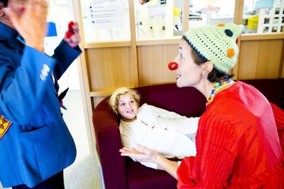 Sara Moberg vilar på soffan i dagrummet, medan sjukhusclownerna Laijla och Sven skojar, trollar och sjunger. Bild: mark hanlon