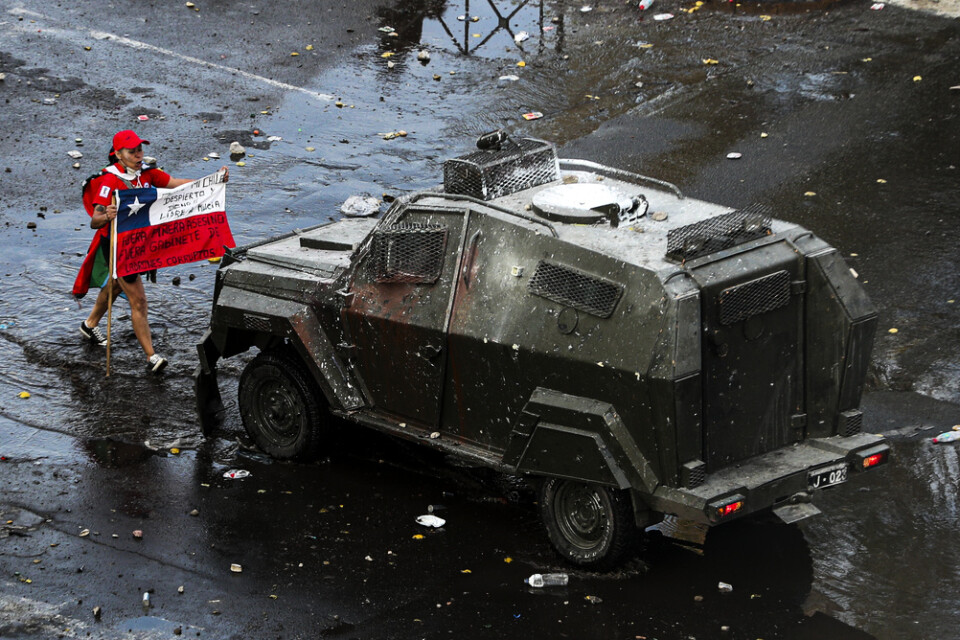 En aktivist håller i den chilenska flaggan framför en militär pansarvagn under en regimkritisk marsch i Santiago den 22 oktober.