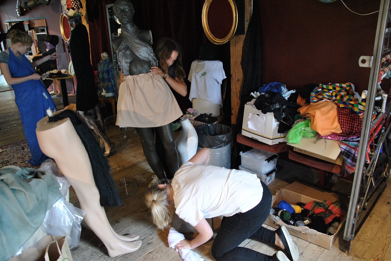 Ella Jordevik och Mimmi Wessman försöker få sin skyltdocka på plats medan Tove Thulin är sin egen skyltdocka när hon syr upp en klänning av tyg de hittat på Barbacka. 							         Foto: Robert Rolf