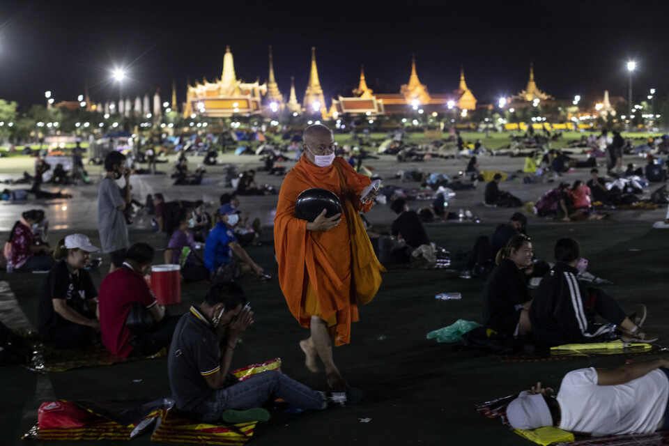 En buddhistmunk delar ut munskydd till de tusentals demonstranter som vägrade lämna Sanam Luang-torget, utanför det kungliga palatset i Bangkok, under natten till söndag.