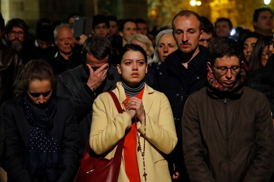 En betraktare knäpper händerna framför Notre-Dame i Paris.