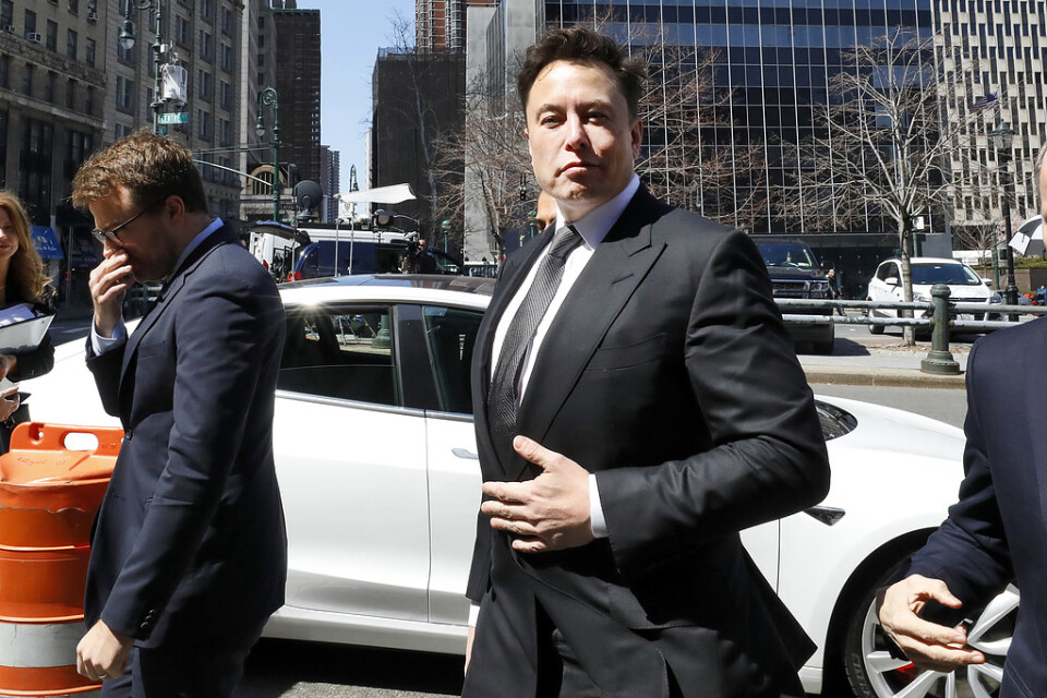 Elon Musk hävdar att Teslas bilar, här en Model 3 bakom honom, ska kunna ta sig fram i trafiken helt själva från och med nästa år. Bilden är från i april.
