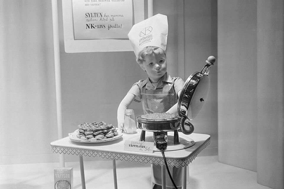 NK’s window in 1950. A dummy, in the shape of a little boy, making waffles.He is wearing a chef’s toque with the NK food hall’s logo.