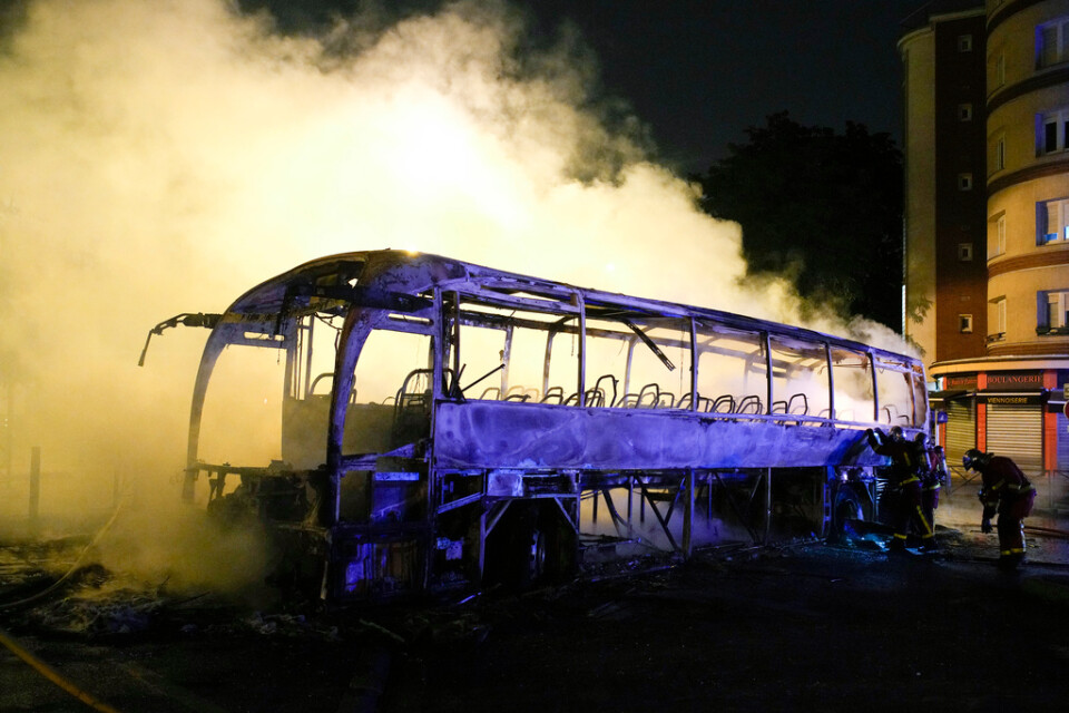 Brandmän släcker glöden i en buss som förstörts i en brand i Nanterre utanför Paris, under natten till lördag.