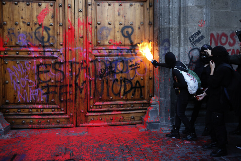 En maskerad deltagare i protesterna vid entrén till presidentpalatset i Mexico City.
