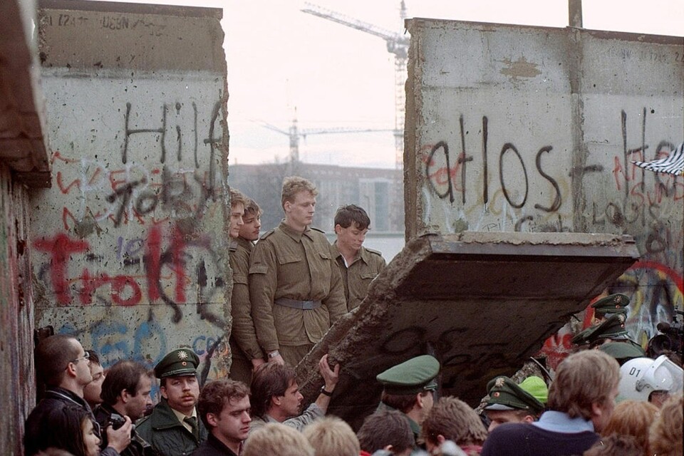 I höst är det 30 år sedan Berlinmuren föll. På bilden står obeväpnade gränssoldater på DDR-sidan när ett segmet av muren faller ned mot Västberlin. Foto: AP Photo/SCANPIX