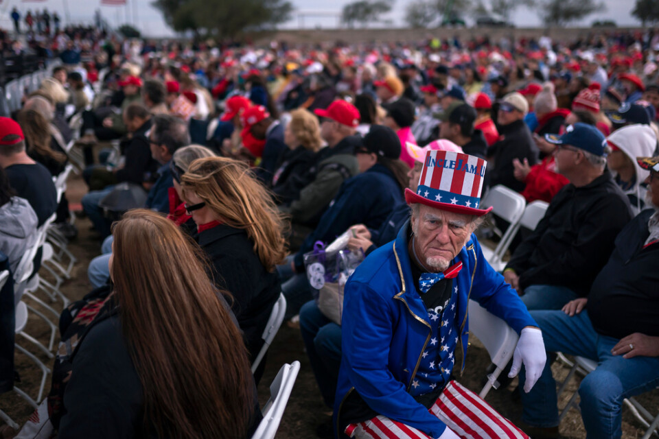 En Trump-anhängare utklädd till Uncle Sam lyssnar medan olika talare värmer upp scenen inför ex-presidentens framträdande.