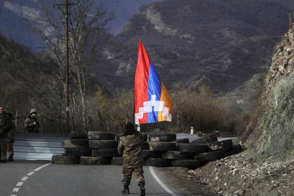 En soldat från Nagorno-Karabach bär den självutropade republiken Artsachs flagga vid en gränskontroll i regionen i november 2020. Separatisternas flagga är en armenisk flagga med ett vitt mönster.