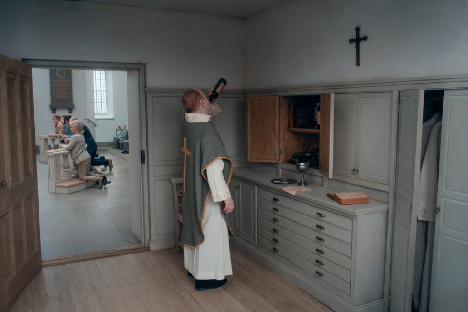 En präst, som häller i sig nattvardsvinet för att dränka ångesten efter att ha förlorat sin tro, avbildas på en av Anderssons bilder. Pressbild.