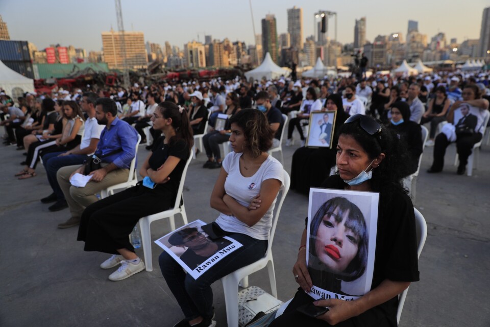 Anhöriga håller upp porträtt av offren för den massiva explosionen för ett år sedan i Beiruts hamn.