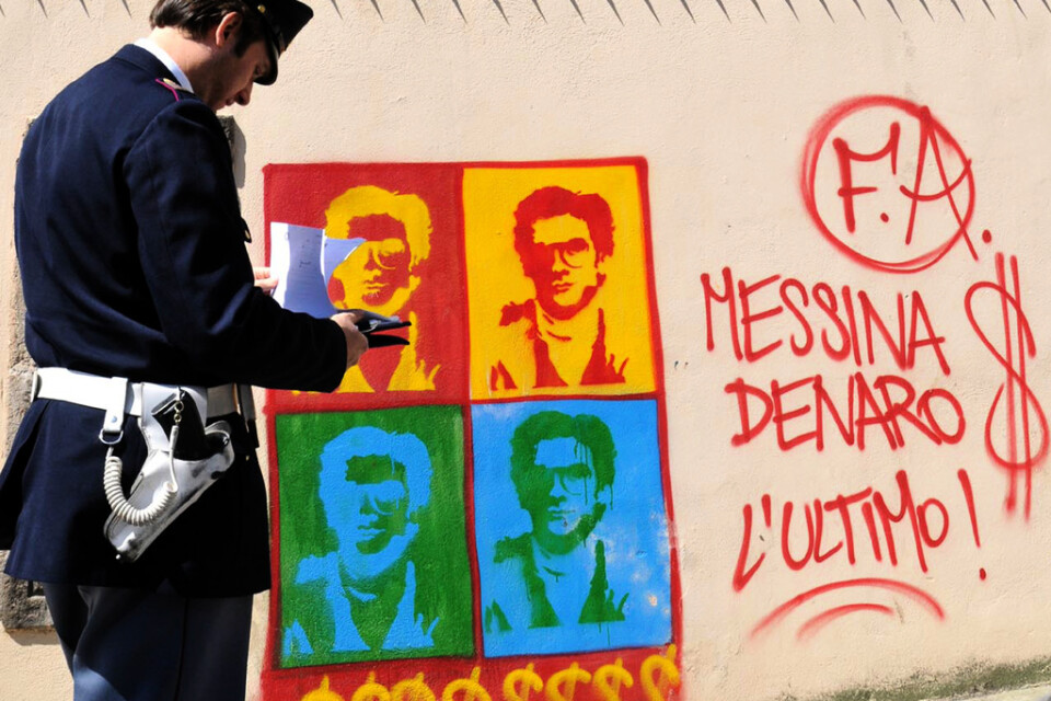 En polis bredvid en väggmålning som porträtterar Matteo Messina Denaro i Palermo 2008.