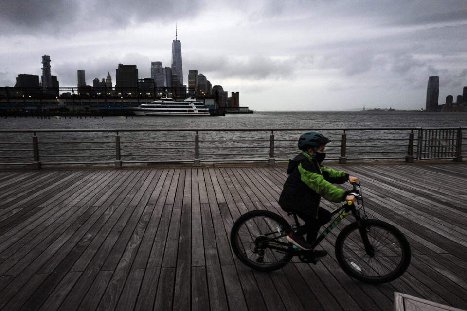En pojke med ansiktsmask är ute och cyklar i Hudson River Park, New York. Pojken har inget med texten att göra.