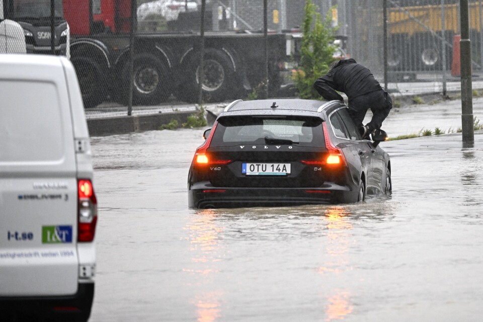 En man klättrar ut en bil som försökte ta sig genom en översvämmad rondell i Arlöv vid den avstängda översvämmade Västkustvägen E6 utanför Malmö, i samband med regnovädret Hans i augusti.