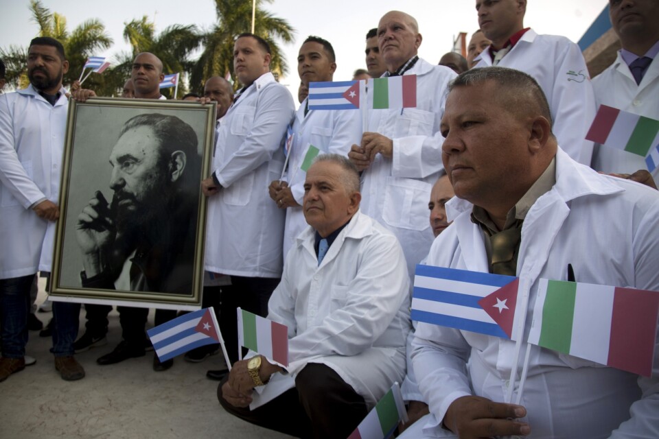En grupp kubanska läkare och vårdarbetare poserar för medier med ett foto av Fidel Castro och italienska och kubanska flaggor i Havanna, före avfärden till Italien, den 21 mars.