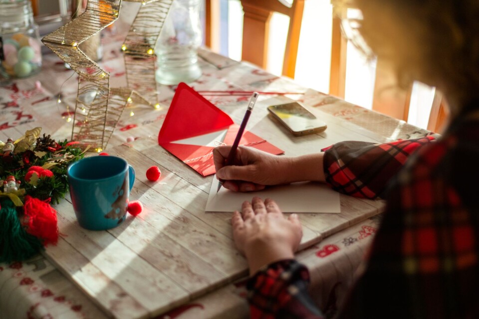 A woman writing a Christmas card on a wooden table
