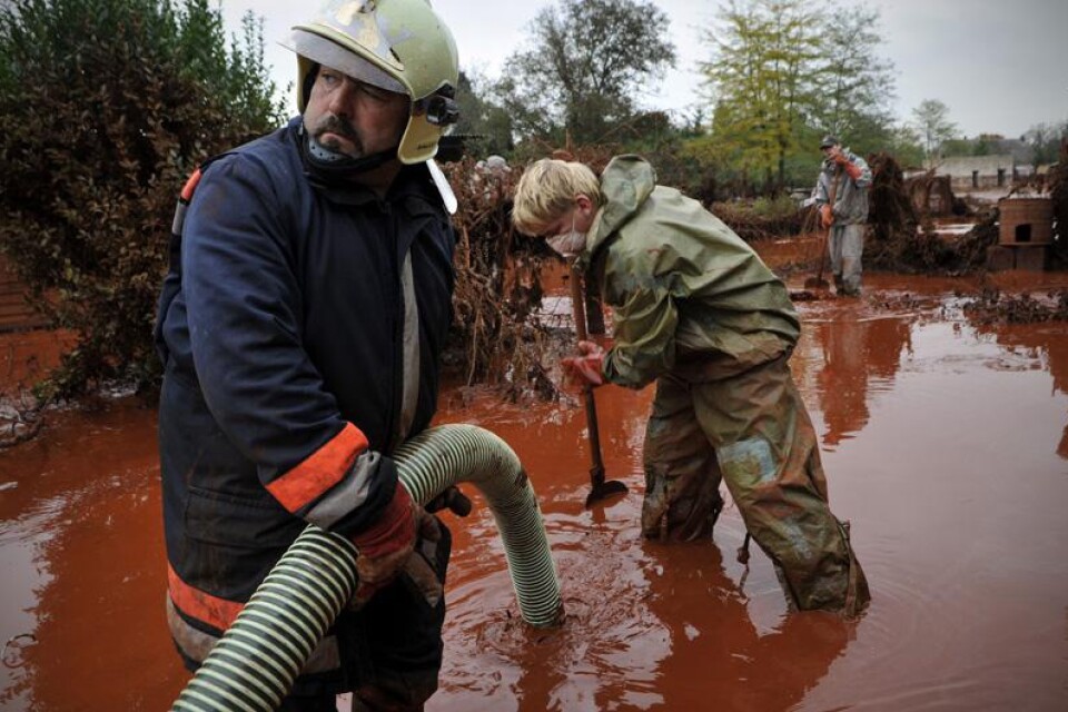 Räddningsmanskap arbetar för att rengöra en gård som översvämmats av det röda, frätande, giftslammet.
