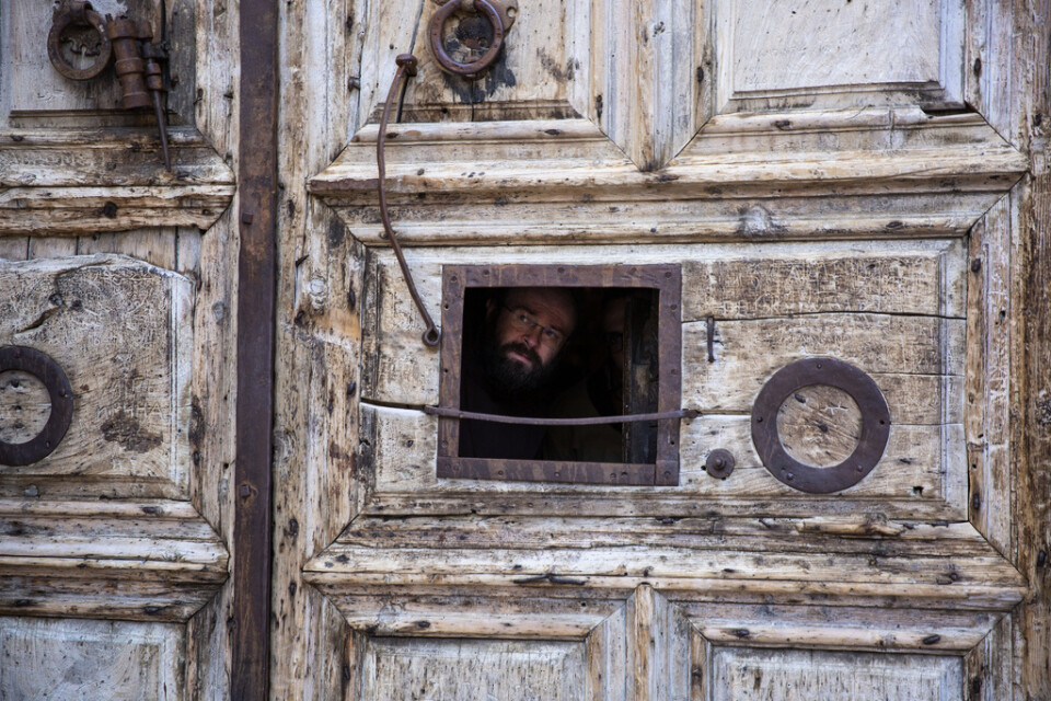 En präst kikar ut genom ett litet fönster i porten till Heliga gravens kyrka i Jerusalem.