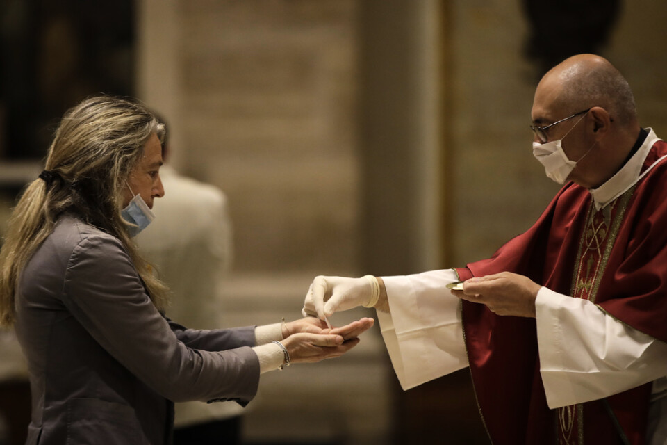 En präst med skyddshandskar delar ut nattvarden till en gudstjänstbesökare i Sankt Eugenio-kyrkan i Rom, som precis som resten av Italiens kyrkor tillåtits öppna.
