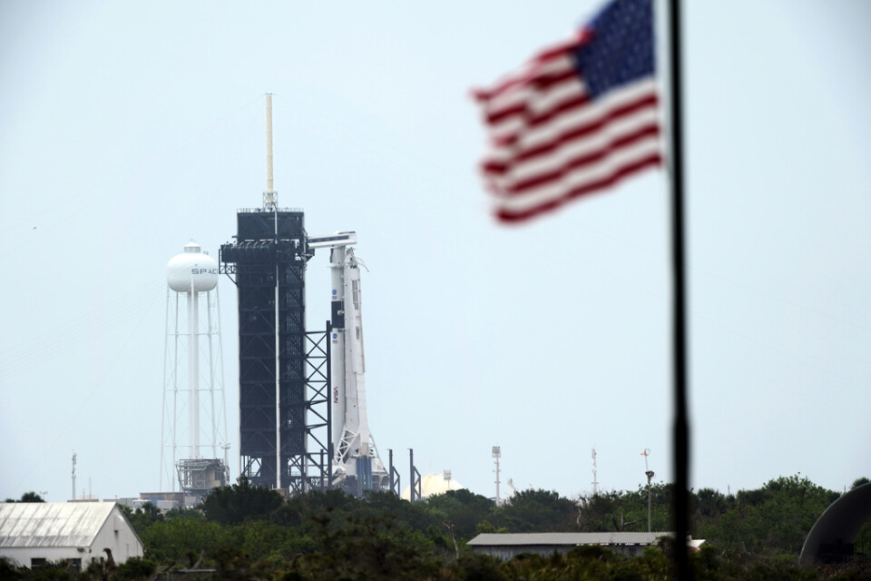 Den startklara Falcon 9-raketen från Space|X, med besättningskapseln Crew Dragon högst upp, till höger om det svarta tornet på Kennedy Space Center.