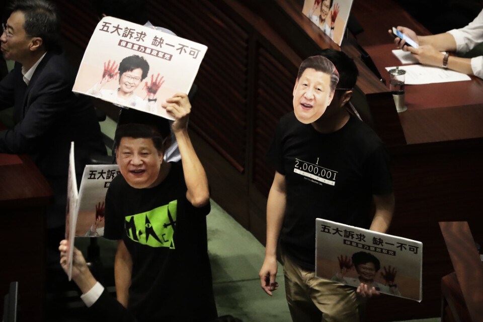 Demokrativänliga parlamentsledamöter bar masker föreställande Kinas president Xi Jinping när de avbröt Carrie Lams tal.