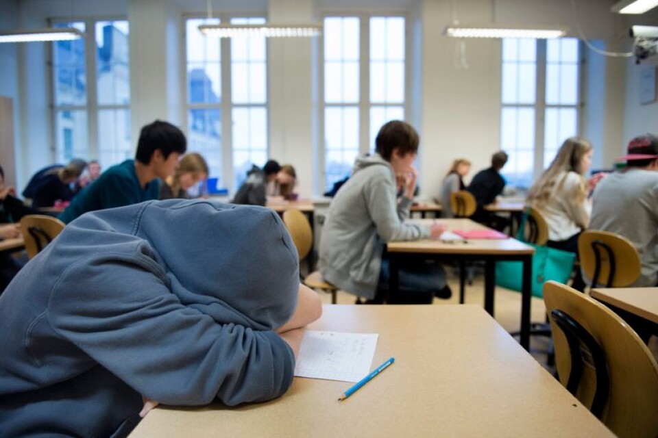 En trött högstadieelev i årskurs 8 sover med huvudet på bänken under en lektion.