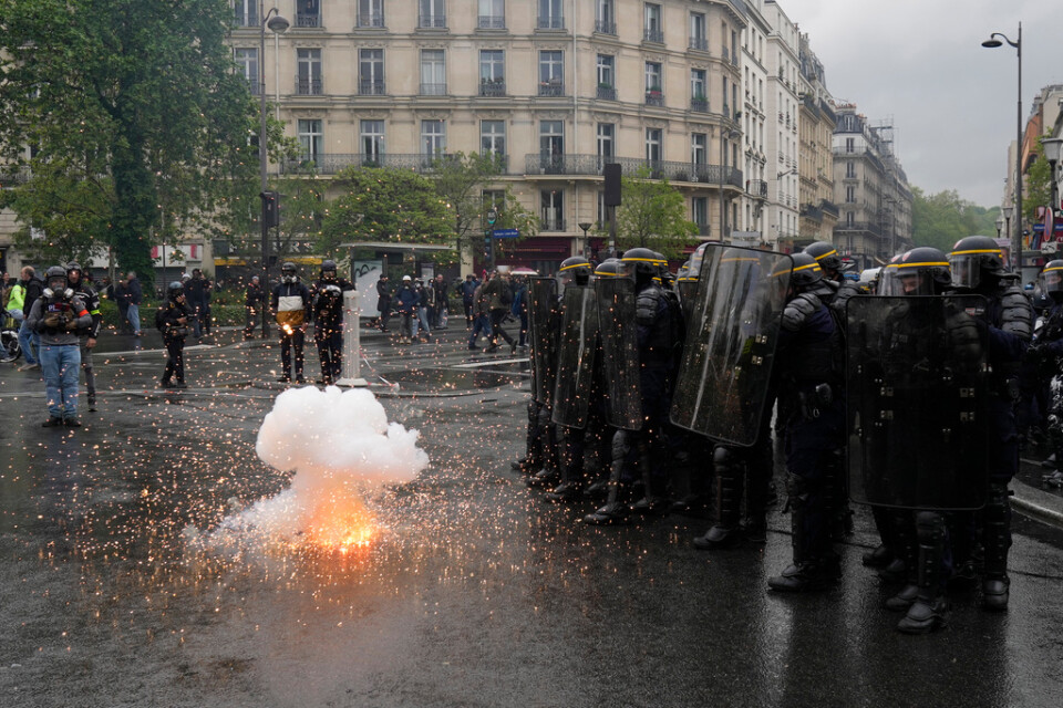 Kravallpoliser skyddar sig från ett sprängämne som kastats mot dem i Paris.