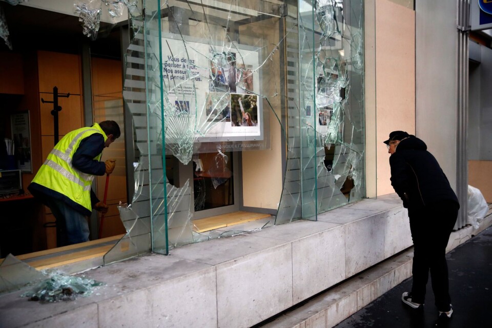 En man städar bort krossat glas inne på en bank i Paris.