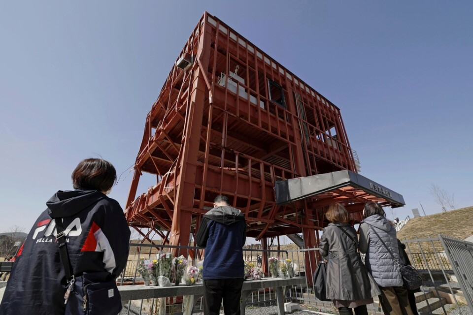 Anhöriga ber på årsdagen i Minamisanriku norr om Fukushima. Den söndertrasade byggnaden tillhörde räddningsverket, och många omkom där i tsunamin 2011.