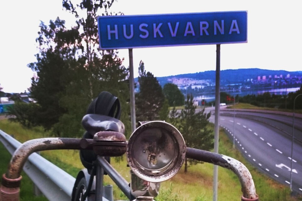 En bild med Husqvarnacykeln framför Huskvarnaskylten.