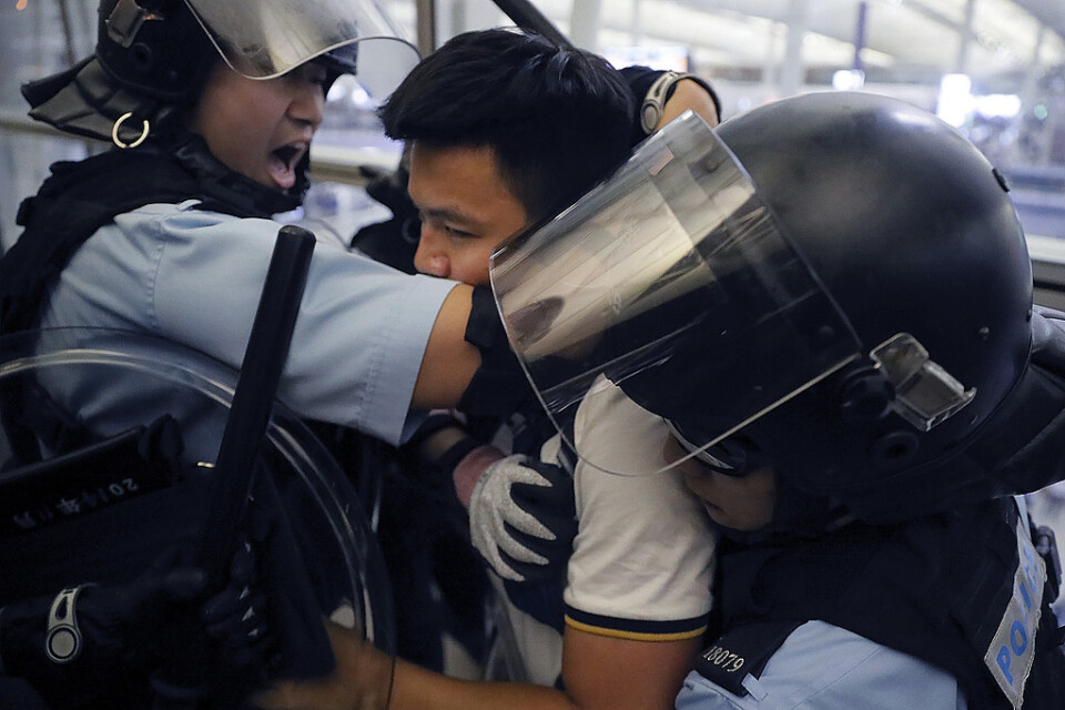Poliser i kravallutrustning griper en demonstrant under tisdagens tumult på Hongkongs internationella flygplats.