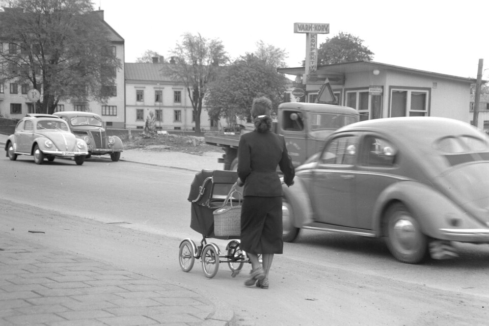 Vilken härlig nostalgibild! Bubblan till vänster med sitt skärmtak, kiosken som säljer Orancia och Pommac, konfektyr och varm korv och sen damen med barnvagnen, klädd i nylonstrumpor med söm bak, dräkt och fotriktiga promenadskor! Vems var kiosken? Hur länge fanns den kvar och vad köpte du där? Tablettask eller klubba? Vi är på Långebro 1954.