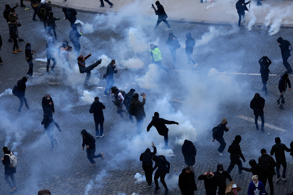 Svartklädda ungdomar försöker sparka bort tårgasbehållare efter en sammandrabbning med polis i Paris.