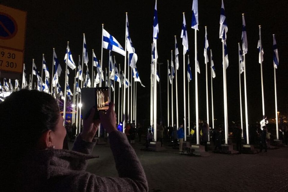 Invid Salutorget i Helsingfors klockan 18 på tisdagskvällen: barn hissade 100 finska flaggor innan nationalsången sjöngs i lätt snöfall. Foto: Lars Näslund.