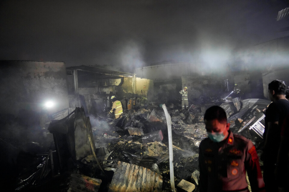 Brandmän inspekterar nedbrunna hus i Jakarta under tidig natt till lördag, lokal tid.