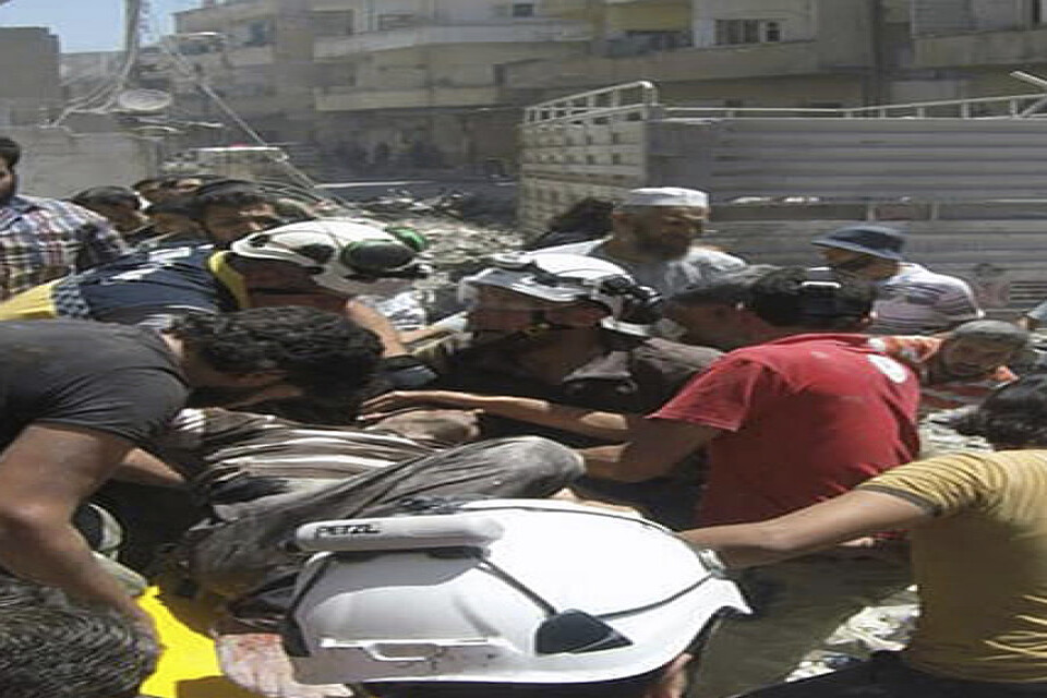 Hjälparbetare från den syriska oppositionella civilförsvarsorganisationen Vita hjälmarna bär en skadad man efter en flygattack mot staden Ariha i Idlib den 28 juli.