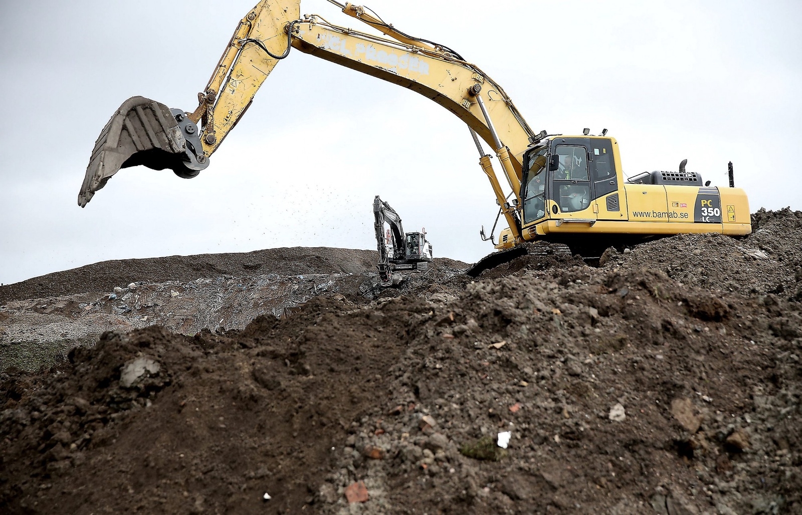 Stora grävmaskiner gräver ner och slätar till efteråt. Så småningom ska den täckas och besås med gräs. Foto: Stefan Sandström