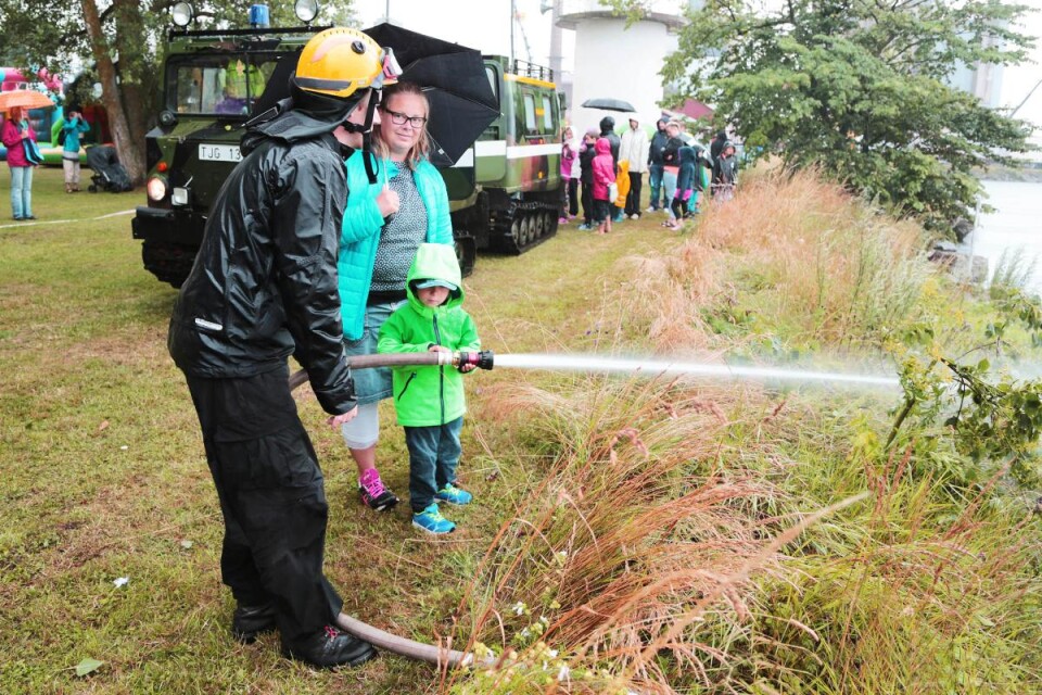 Brandmannen Patrik Norlander låter Grayson Dauman från Arontorp spola vatten med räddningstjänstens slang. Mamma Kathrine är åskådare. Foto: Roland Andersson