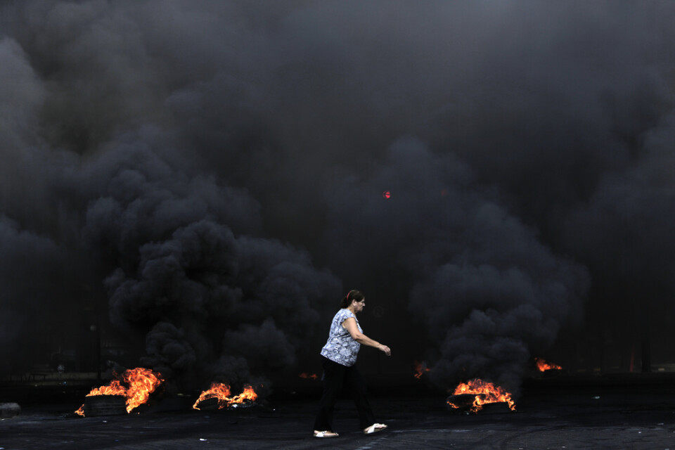 En kvinna går förbi brinnande bildäck under protesterna i Beirut.