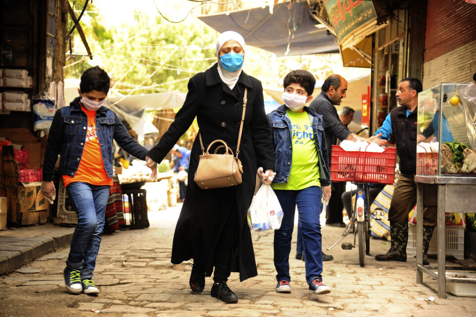 En syrisk kvinna och hennes två söner på en marknad i huvudstaden Damaskus – där munskydd blivit en allt vanligare syn.