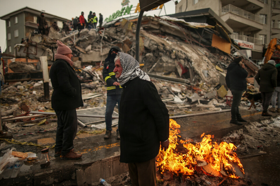 Människor försöker värma sig runt en eld vid av de många raserade byggnaderna i den turkiska staden Malatya.